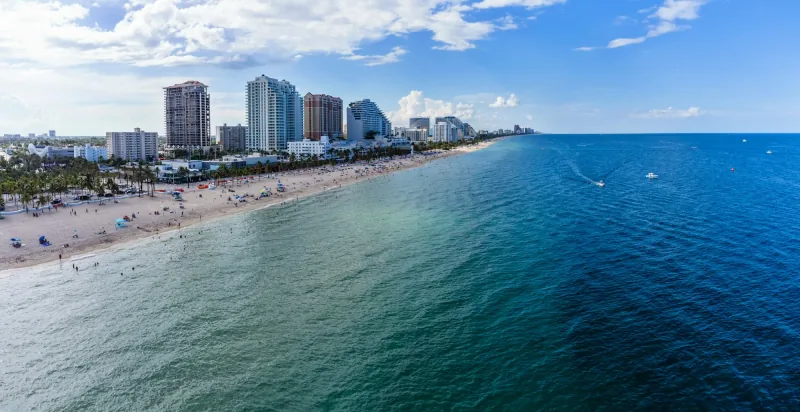The Fort Lauderdale shoreline seen from the water, with the beachfront towers running away along the sand under a clear sky.